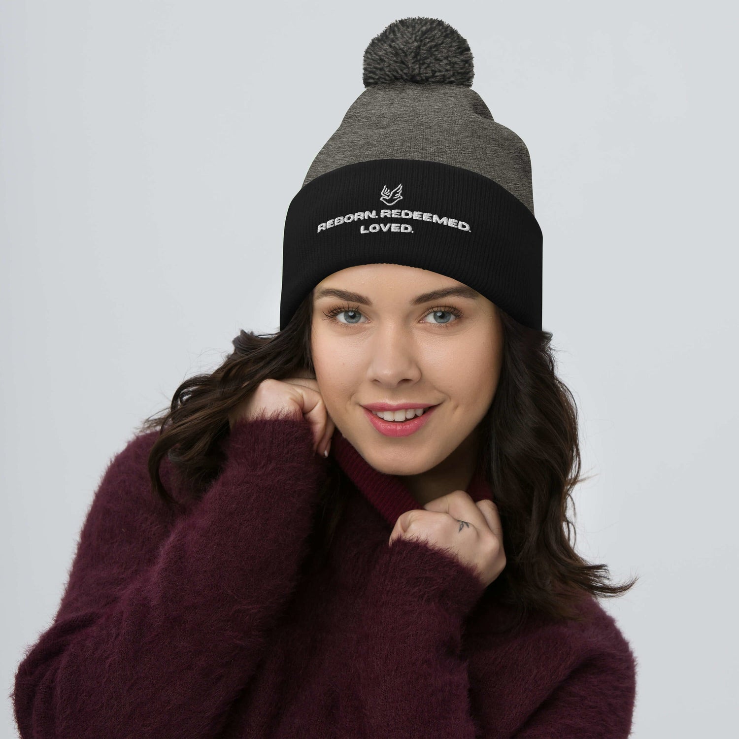 Woman wearing a Christian pom pom beanie that reads redeemed, reborn, and loved. 